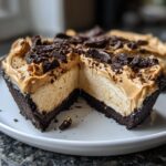 A cross-section view of a no-bake peanut butter pie showing the creamy filling, dark chocolate crust, and cookie crumble topping.