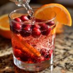 Close-up of sparkling liquid being poured over cranberries and an orange slice in a glass for non-alcoholic christmas punch.
