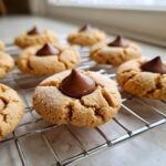 Close-up of a freshly baked peanut butter blossom cookie, topped with a chocolate kiss, cooling on a wire rack.