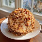 A perfectly shaped cheese ball recipe coated entirely in chopped pecans, sitting on a white plate.