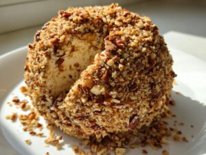A close-up of a pineapple cheese ball coated entirely in chopped nuts, with one slice cut out.