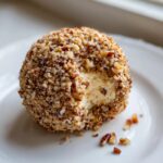 A creamy pineapple cheese ball coated heavily in chopped nuts, with a bite taken out showing the interior.