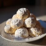 A tempting stack of freshly baked russian tea cakes heavily dusted with powdered sugar on a white plate.