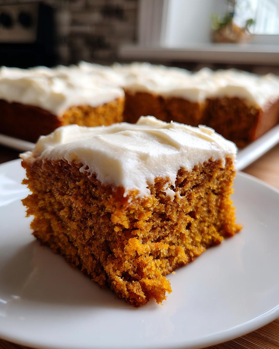 A close-up of a moist slice of pumpkin bars with cream cheese frosting on a white plate.