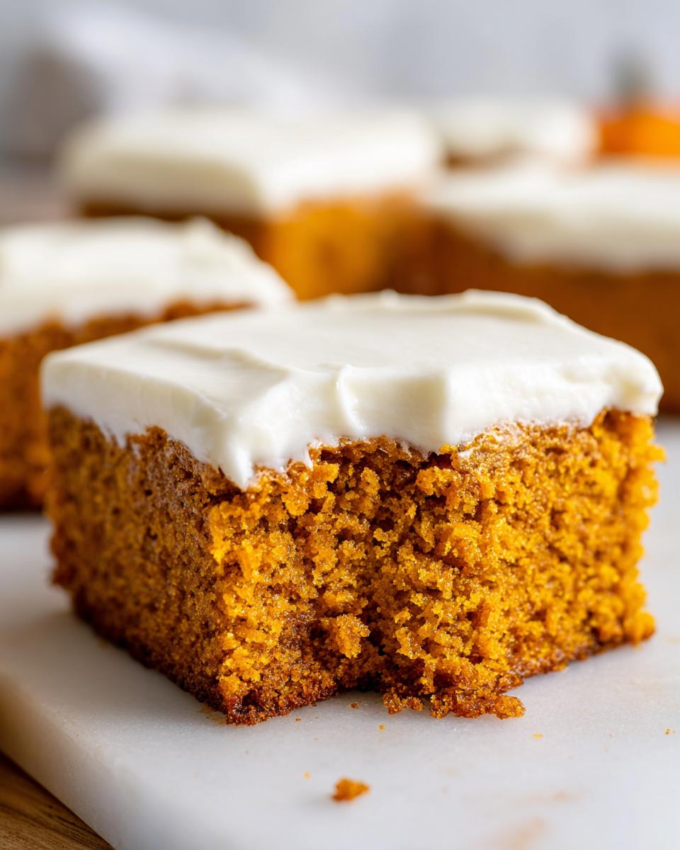 A close-up shot of a moist, orange pumpkin bars with cream cheese frosting, showing texture.