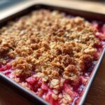 Close-up of a freshly baked rhubarb crisp with a golden, crunchy oat topping and bubbling red fruit filling.