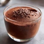 Close-up of rich, dark chocolate mousse served in a clear glass, topped with chocolate shavings.