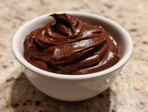A close-up of thick, glossy homemade chocolate pudding swirled high in a small white bowl.