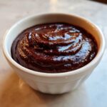 A close-up of rich, glossy homemade chocolate pudding swirled in a small white bowl.