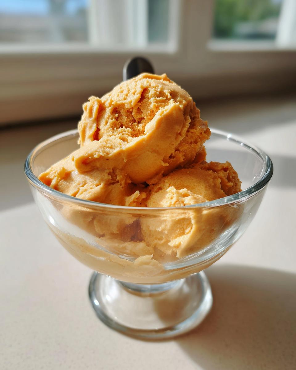 Three scoops of light orange pumpkin fluff dessert served in a clear glass sundae dish.