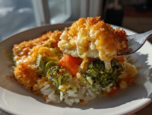 A fork lifting a cheesy, crunchy bite from a creamy vegetable casserole served over rice.