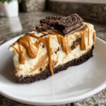 A tempting slice of biscoff cheesecake with a thick crust, caramel drizzle, and cookie topping on a white plate.