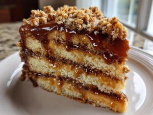Close-up of a slice of caramel crunch cake showing three layers of sponge cake, caramel filling, and a crunchy topping.
