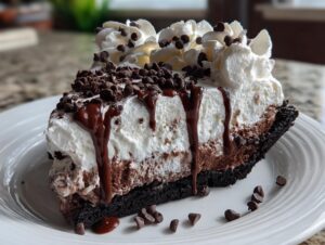 A decadent slice of chocolate ice cream pie topped with whipped cream, chocolate drizzle, and mini chocolate chips.