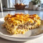 A hearty slice of sour cream beef noodle casserole featuring layers of egg noodles, ground beef, and a melted, bubbly cheddar cheese topping.