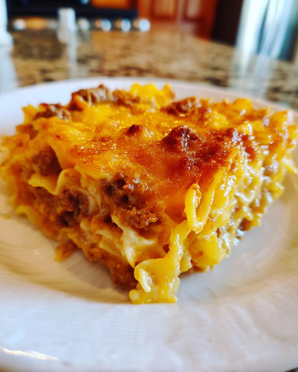 Close-up of a warm, cheesy slice of sour cream beef noodle casserole with browned topping.