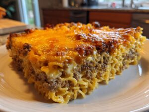 A thick slice of baked sour cream beef noodle casserole topped with melted, browned cheddar cheese.