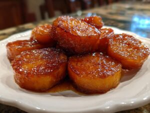 A close-up of thick-cut, glistening Southern candied yams coated in a rich, dark brown syrup on a white plate.