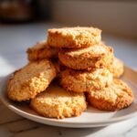 A close-up stack of golden brown, crumbly butter cookie treats piled high on a white plate.