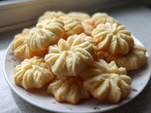 A close-up pile of golden, star-shaped butter cookies arranged on a white plate.