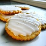 Close-up of a golden sugar cookie topped with thick, glossy white sugar cookie icing and sprinkled with coarse sugar.