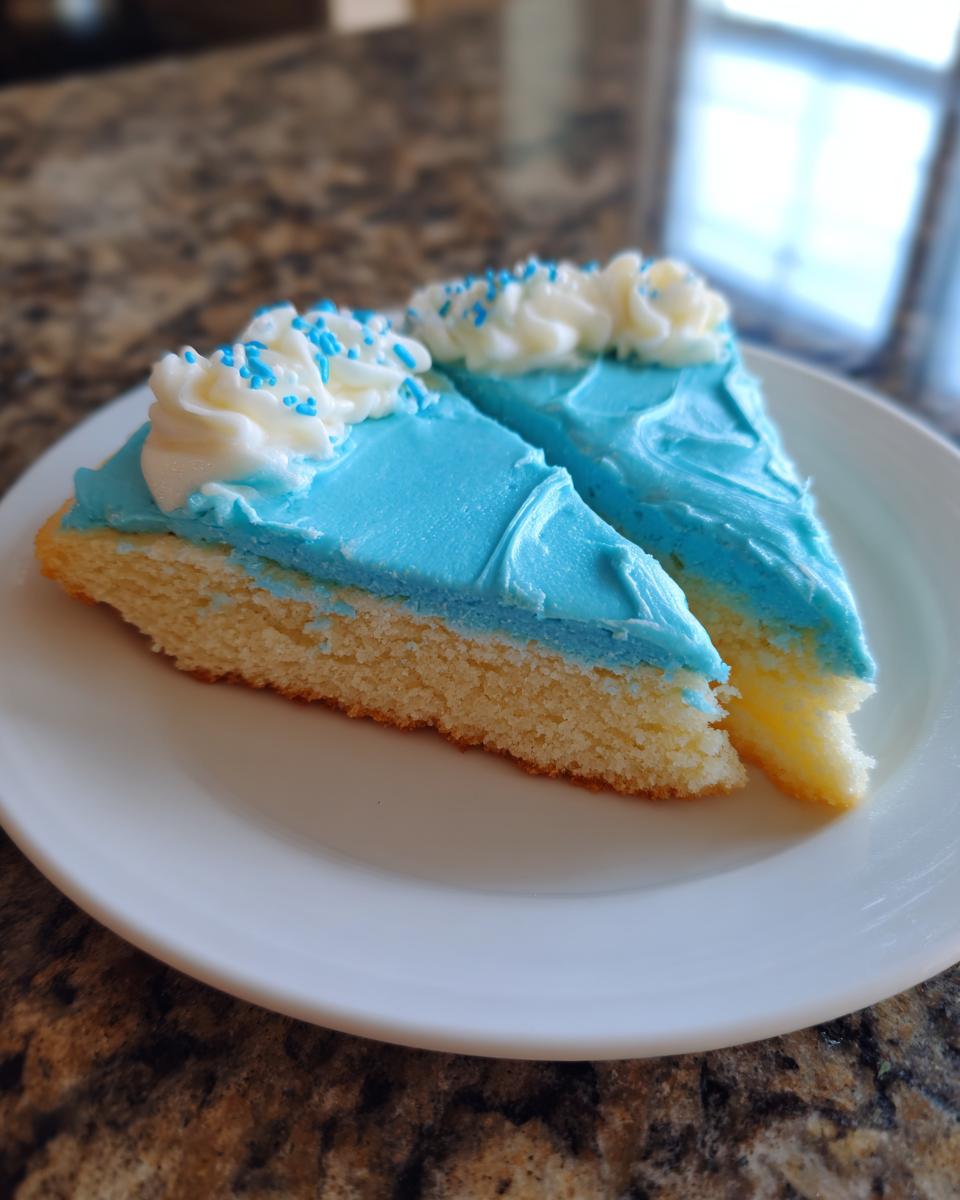 Two slices of sugar cookie cake topped with bright blue sugar cookie icing that hardens, white frosting swirls, and blue sprinkles.