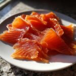 Close-up of bright orange, thinly sliced smoked salmon pieces arranged on a white plate.