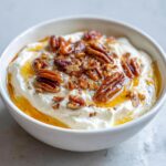 A white bowl filled with creamy whipped goat cheese, drizzled with honey and topped with toasted pecans.