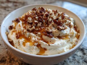 A white bowl filled with fluffy whipped goat cheese, drizzled with honey and topped with chopped pecans.