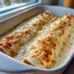 Two freshly baked white chicken enchiladas covered in creamy white sauce and bubbly, browned cheese.