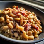 Close-up of creamy black eyed peas topped with savory pieces of ham in a dark bowl.