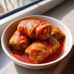 Four savory cabbage rolls smothered in bright red tomato sauce served in a white bowl.