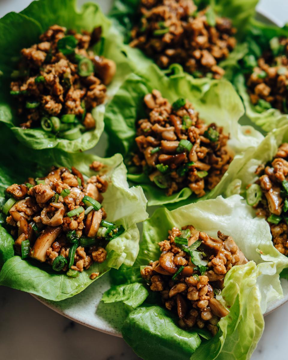 Close-up of several fresh chicken lettuce wraps filled with savory ground chicken and mushroom mixture, garnished with green onions.