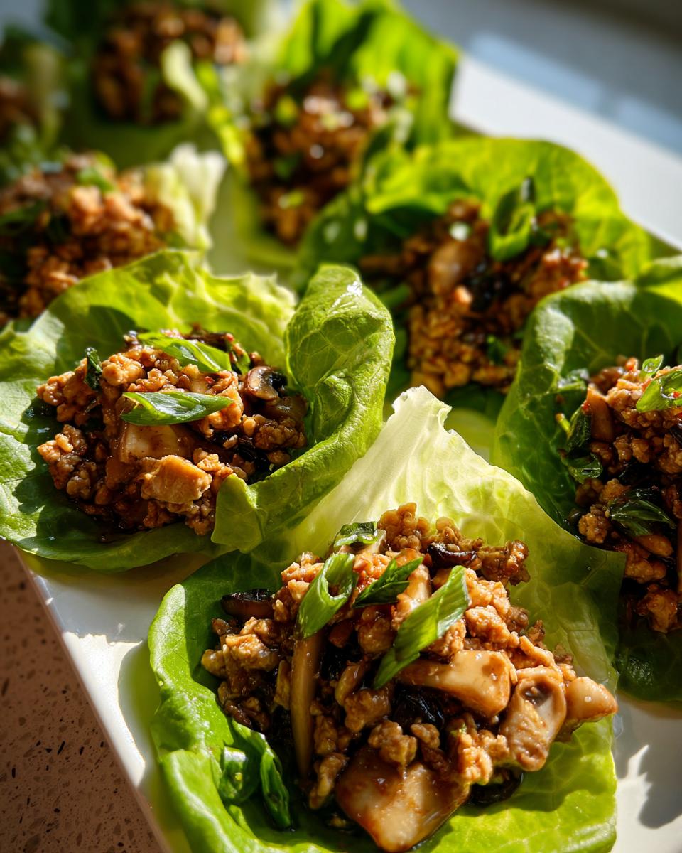 Close-up of several fresh chicken lettuce wraps filled with savory ground chicken and mushrooms, garnished with green onions.