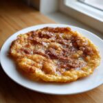 A close-up of a freshly fried, golden-brown buñuelos generously topped with cinnamon sugar and glaze.