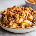 Close-up of a serving of apple crisp recipe showing tender baked apples under a thick, golden-brown, crunchy oat topping.