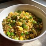 A white bowl filled with healthy cauliflower fried rice mixed with scrambled egg and topped generously with chopped green onions.