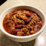 Close-up of a white bowl filled with rich, thick high protein chili featuring ground meat and dark red kidney beans.