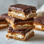 A stack of three rich buckeye graham crackers layered with marshmallow and caramel, topped with chocolate.