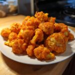 A white plate piled high with crispy, bright orange buffalo cauliflower bites, glistening with sauce.