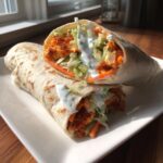 Two halves of a crunchy buffalo chicken wrap filled with lettuce, carrots, and ranch dressing.