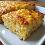 Close-up of a square slice of cheesy corn casserole, showing whole corn kernels throughout the moist texture.