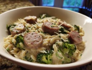 Close-up of a creamy bowl of chicken sausage and broccoli orzo topped with grated cheese.