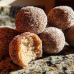 A close-up of several soft cinnamon sugar snowball cookies, one of which has a bite taken out, revealing the crumbly interior.