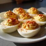 A close-up of six halves of classic deviled eggs, piped high with creamy filling and sprinkled generously with paprika.