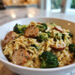 Close-up of a bowl filled with creamy chicken sausage and broccoli orzo, featuring sliced sausage and bright green florets.
