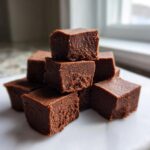 A stack of rich, dark chocolate fudge squares showing a creamy, slightly granular texture.