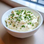 A white bowl filled with creamy, rich clam dip, generously garnished with chopped fresh green chives.