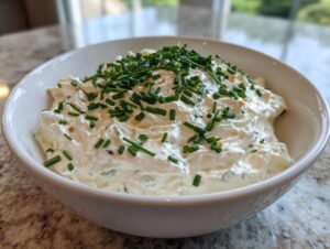 A white bowl filled with creamy clam dip, generously garnished with freshly chopped green chives.