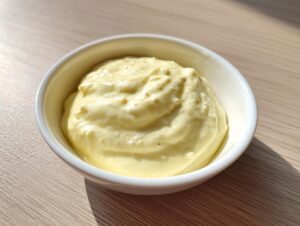 A close-up of thick, creamy, pale yellow homemade garlic aioli served in a small white bowl.